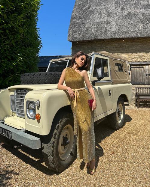Woman in gold dress posing next to a vintage Land Rover.