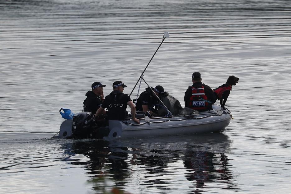 Police officers and a police dog in a boat searching a lake.