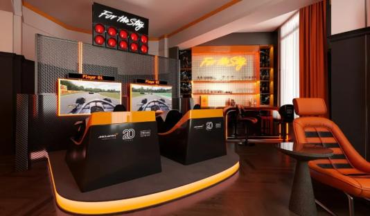 Illustration of a McLaren-themed Hilton hotel suite with twin F1 simulators, a bar, and orange decor.