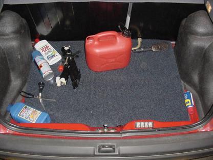 The trunk of a red Ford Fiesta containing a red petrol can, scissors, and other items.