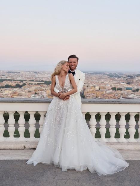 Bride and groom embracing on a balcony overlooking a city.