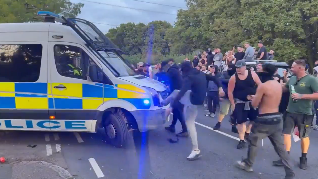 A police van surrounded by a crowd of people.