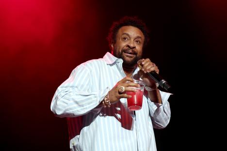 Shaggy performing onstage with a microphone and a drink.