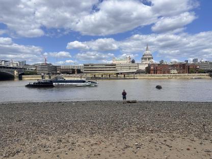 Person standing on a pebble beach looking at St. Paul's Cathedral across the Thames River.