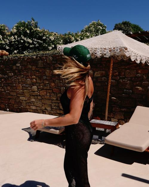 Woman in a black dress and green baseball cap walking by a pool.