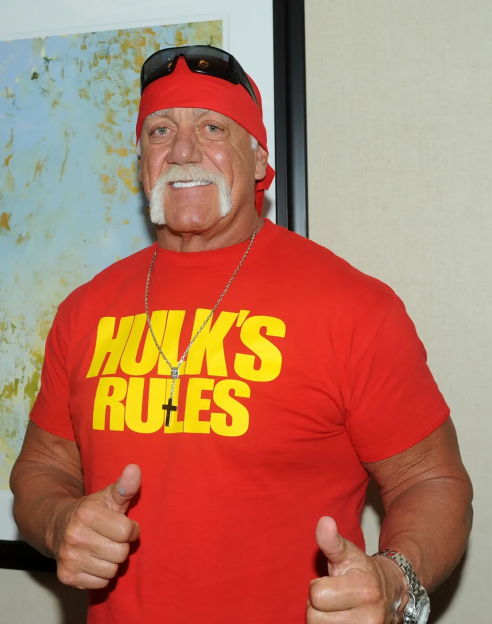 Hulk Hogan giving a thumbs up, wearing a red shirt that says