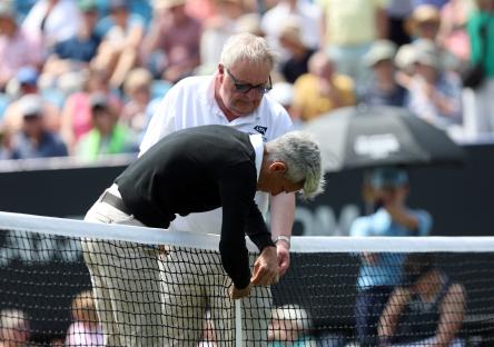 Umpire and groundstaff repairing a tennis net.