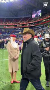 John Textor, wearing a cowboy hat, walks on a soccer field with flight attendants.