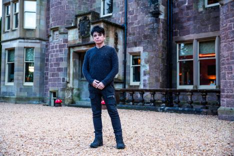 Gary Numan standing outside a stone building.
