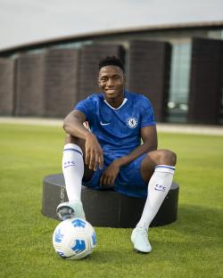 Dario Essugo, new Chelsea signing, sits on a training ground with a soccer ball.