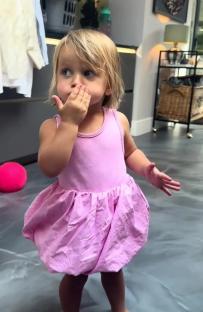 Toddler girl in pink dress covering her mouth.