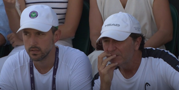 Two men wearing white hats and shirts seated at a tennis match.