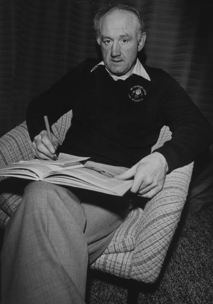 Black and white photo of Ray French, a BBC television rugby league commentator, sitting in a chair and reading.