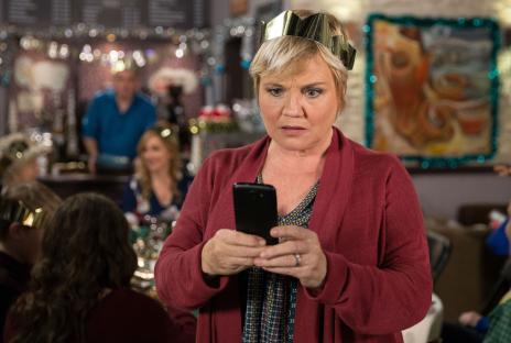 Woman wearing a paper crown looking concerned at her phone.