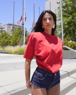 Woman in red shirt and denim shorts outdoors.