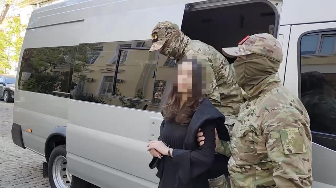 A woman in handcuffs being escorted by two armed officers into a van.