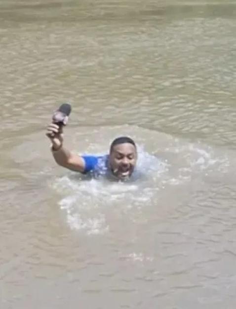 Reporter in river, holding microphone.