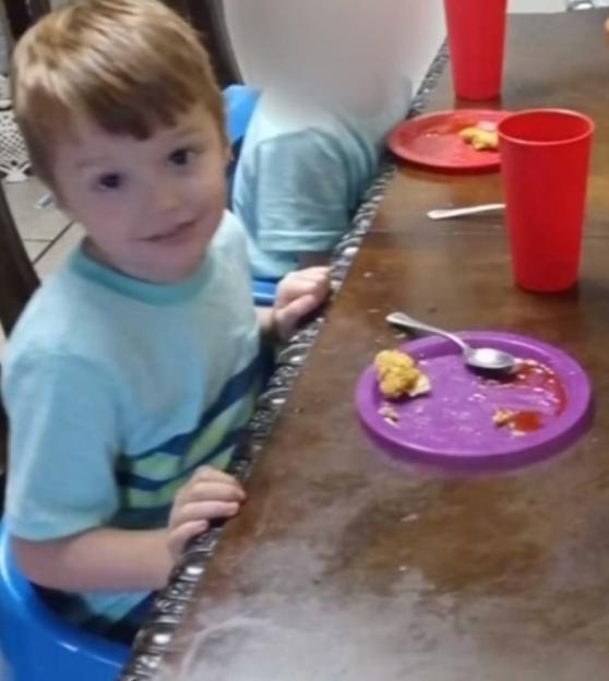 Young boy sitting at a table eating chicken nuggets.