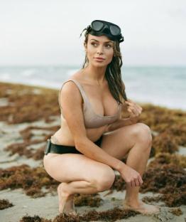Woman in a swimsuit and diving mask crouching on a beach.