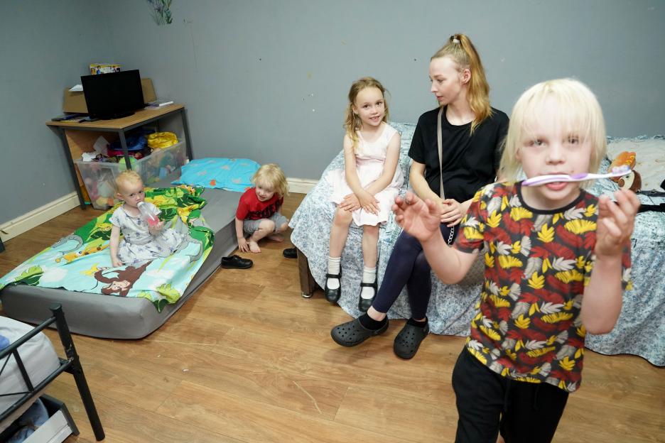 A mother and her four young children in a cluttered room.