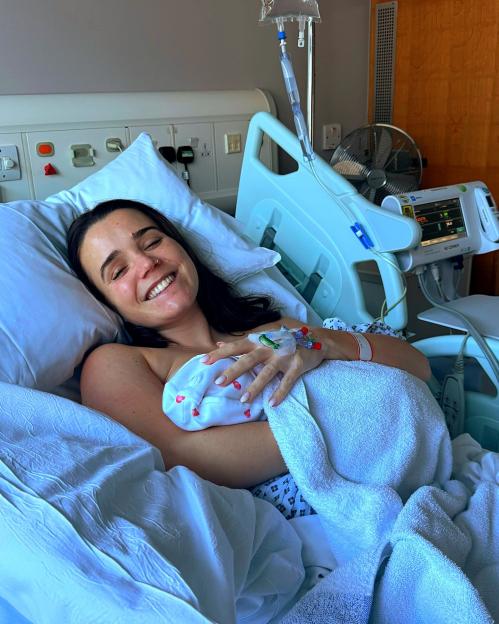 A smiling mother holding her newborn baby in a hospital bed.