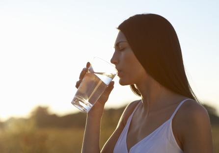 Woman drinking water outdoors at sunset.