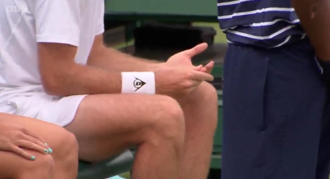 Close-up of a man's legs and hands; he's wearing a white wristband with a logo.