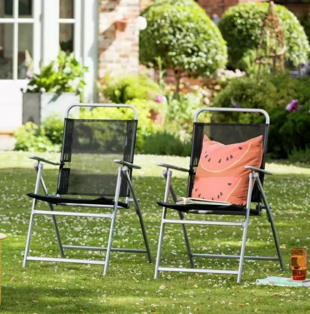 Two black mesh folding chairs on a lawn, one with a watermelon patterned cushion.