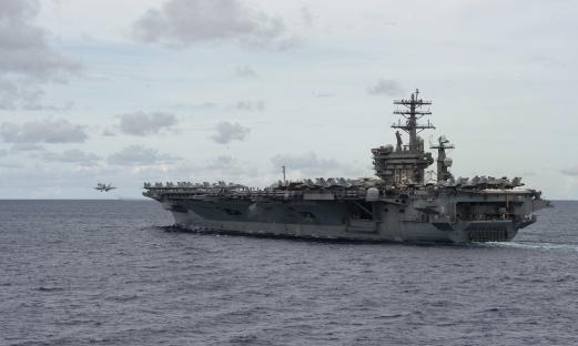 USS Nimitz aircraft carrier at sea with an F/A-18E Super Hornet taking off.