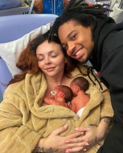 A woman and man holding their newborn twin girls in a hospital bed.