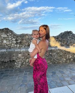 Woman holding a baby in front of a stone wall.