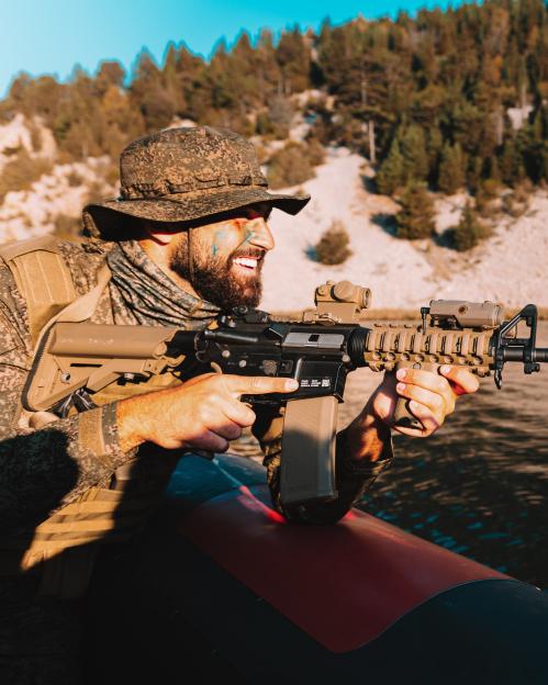 A soldier in camouflage holding a rifle in a boat.