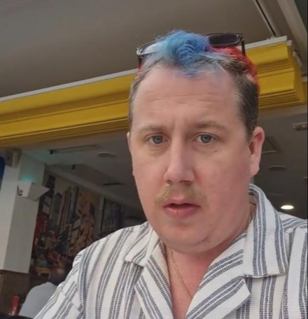 Man with blue and red hair reviewing a cheap full English breakfast.