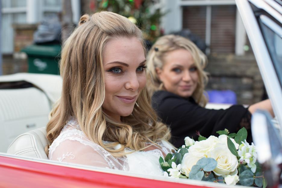 Two women in a convertible, one in a wedding dress.