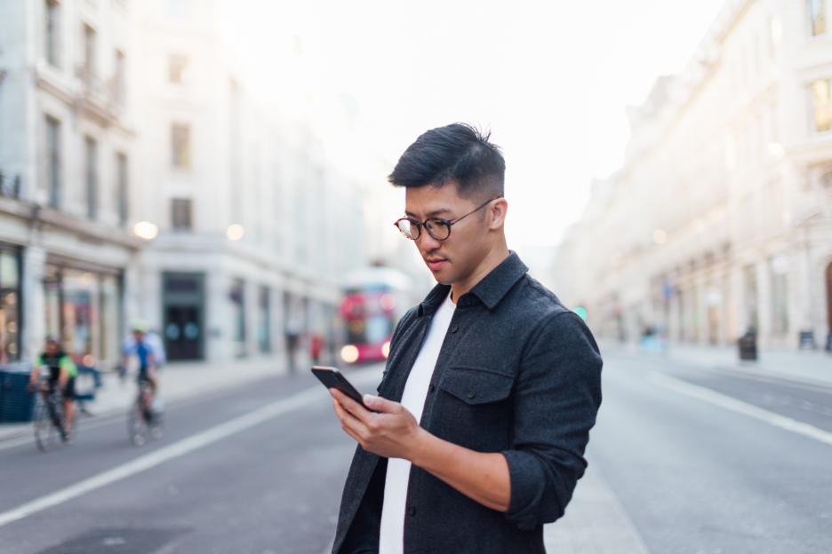 Young man using smartphone on city street.