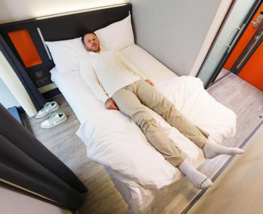 A tall basketball player lying on a small hotel bed.