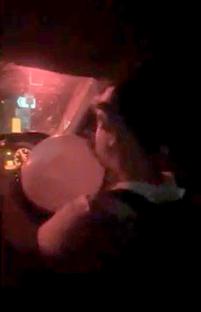 Screengrab of a person driving a car and inhaling nitrous oxide.