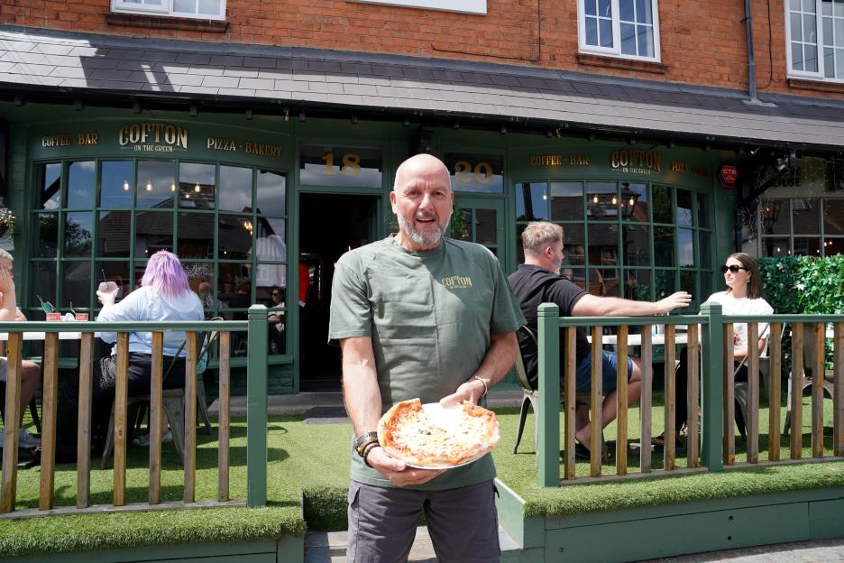 A man holding a pizza outside Cotfon on the Green, a coffee bar and pizza bakery.