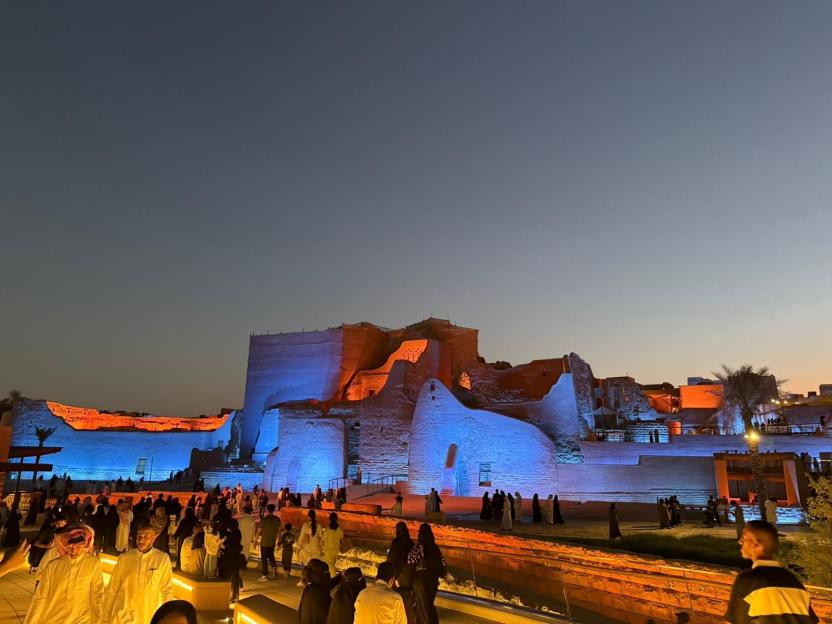 Nighttime view of illuminated ancient ruins with people walking nearby.