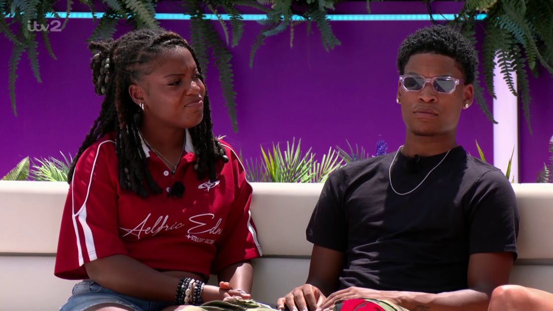 Two people sitting on a couch, looking serious.