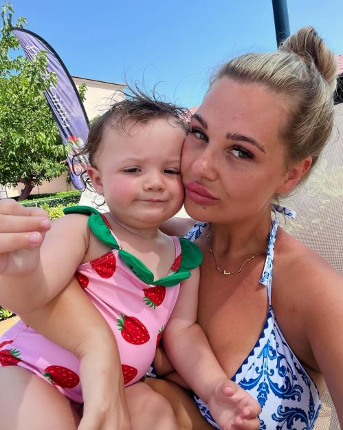 Woman holding a baby wearing a strawberry swimsuit.