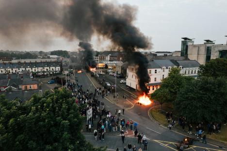Aerial view of riots in Ballymena, Northern Ireland, showing smoke and fire.