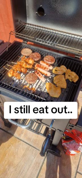 Burgers, sausages, chicken, and skewers grilling on a barbecue.