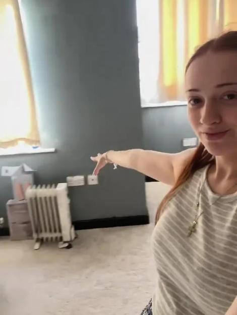 A young woman points to a sparsely furnished room.