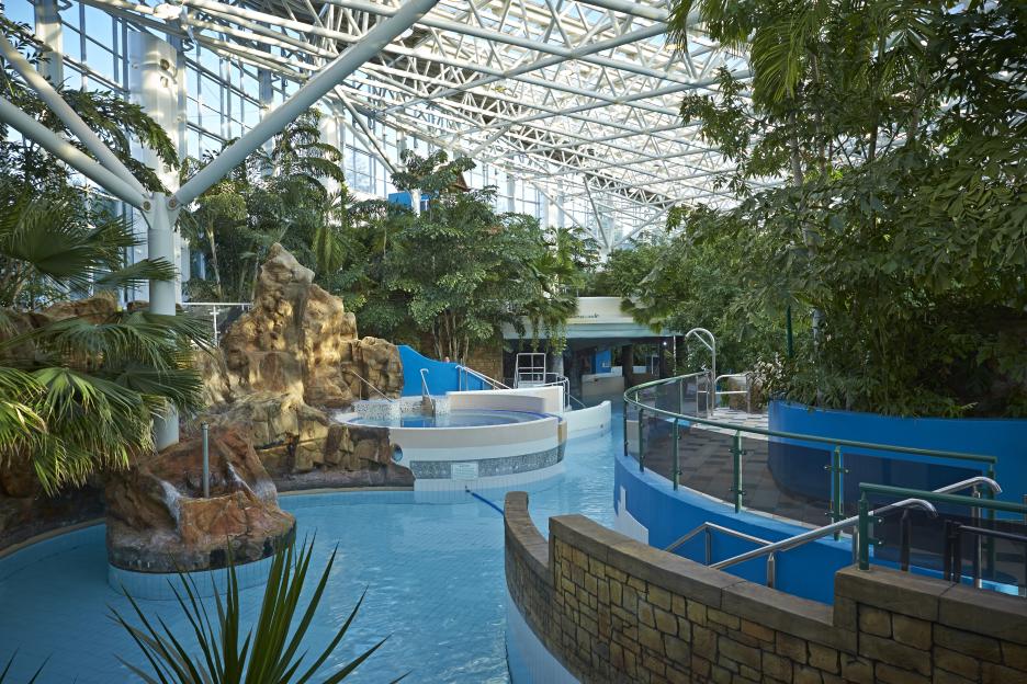 Indoor subtropical swimming paradise with a winding pool and tropical plants.