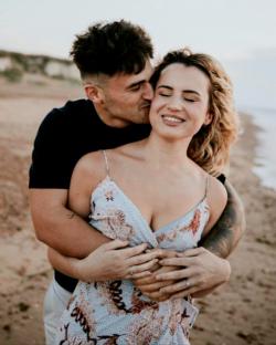 A man kissing a woman on the cheek, embracing her on a beach.