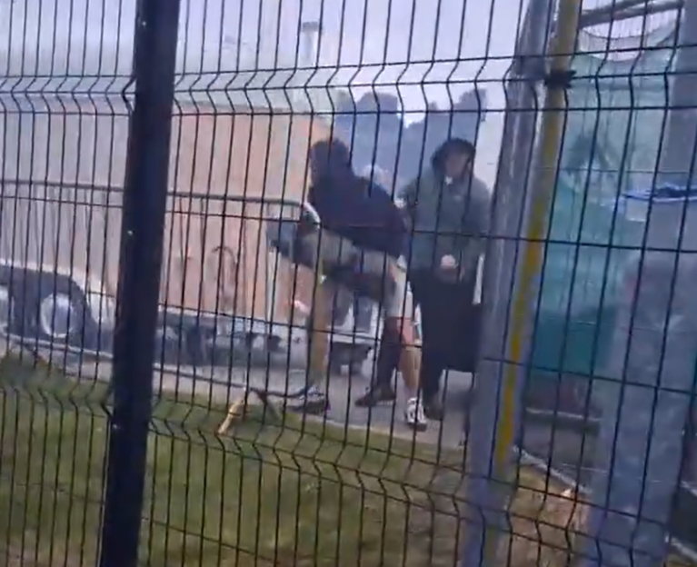 People launching fireworks over a fence.