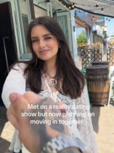 A woman and man holding hands; they met on a reality dating show and are moving in together.