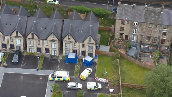 Aerial view of a murder scene, with police vehicles and forensic tents.