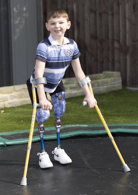 Boy with prosthetic legs and crutches on a trampoline.